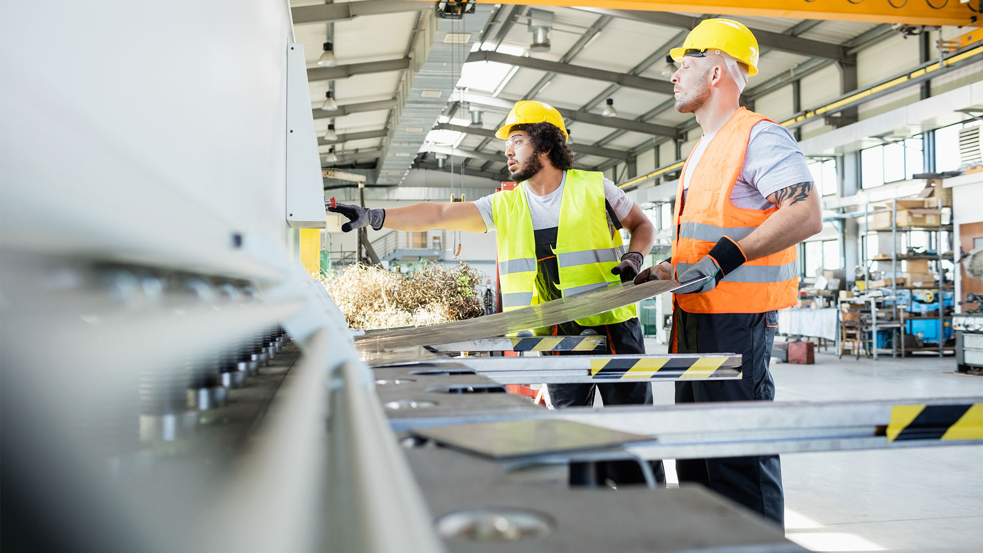 Mannen (met veiligheidskleding aan) aan het werk in fabriek met machines