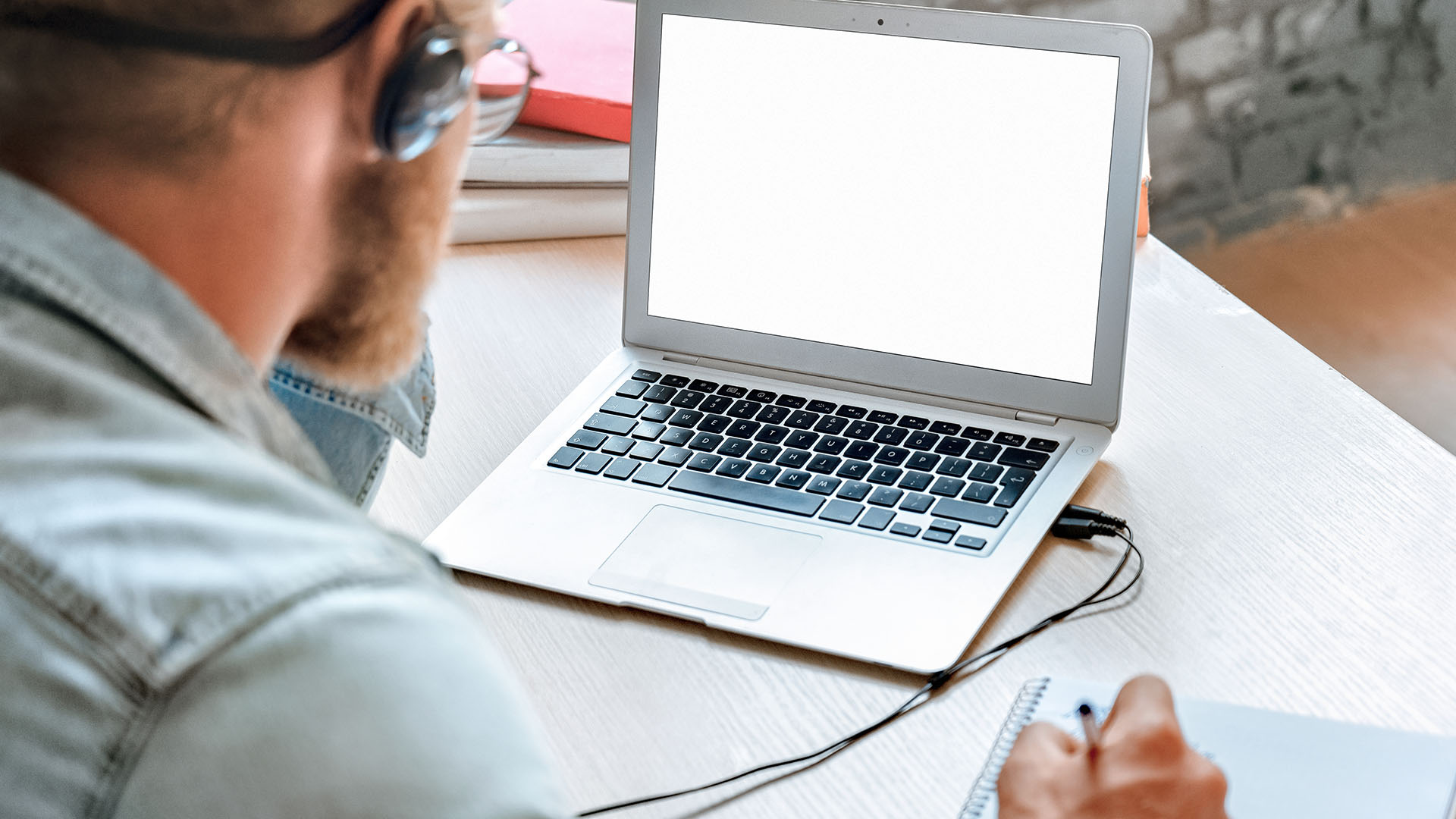 Man achter laptop met schrijfblok