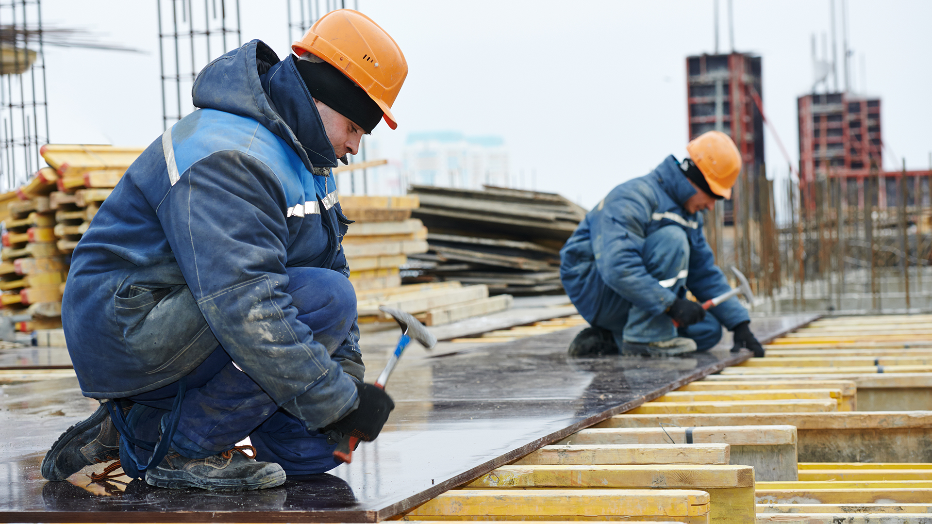 Twee bouwvakkers, warm aangekleed met veiligheidshelm op, aan het werk op een gebouw in aanbouw