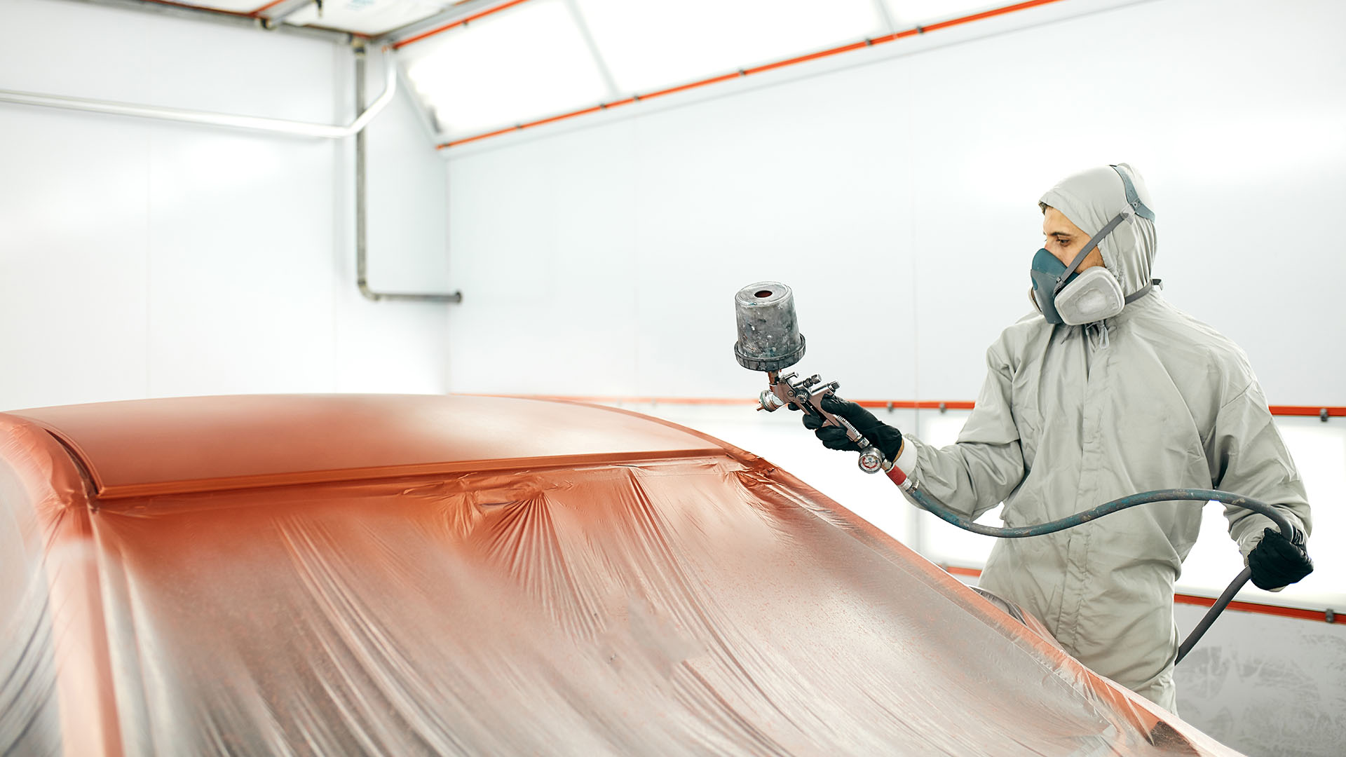 Man met beschermende kleding en masker spuit een auto met behulp van compressor.