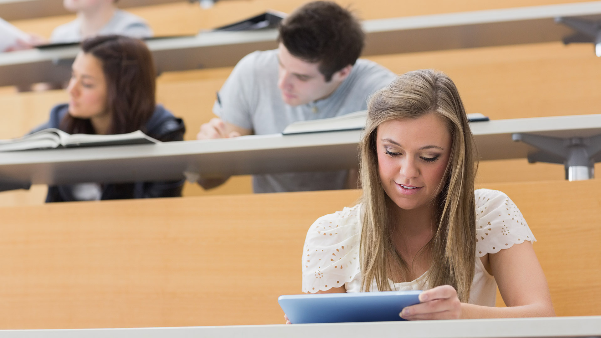 Student zit in de collegezaal terwijl hij een tablet-pc vasthoudt en gebruikt om aantekeningen te maken