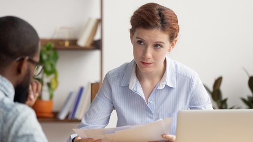 Vrouw en man in gesprek met papieren en een laptop