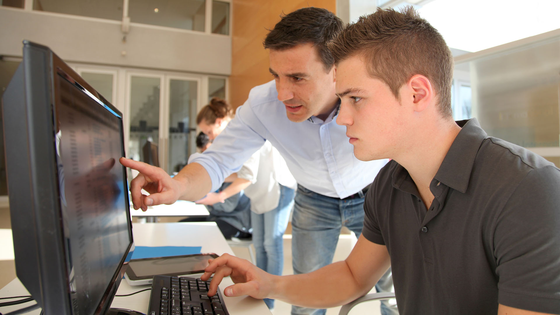 Een docent wijst op het computerscherm om de leerling iets duidelijk te maken