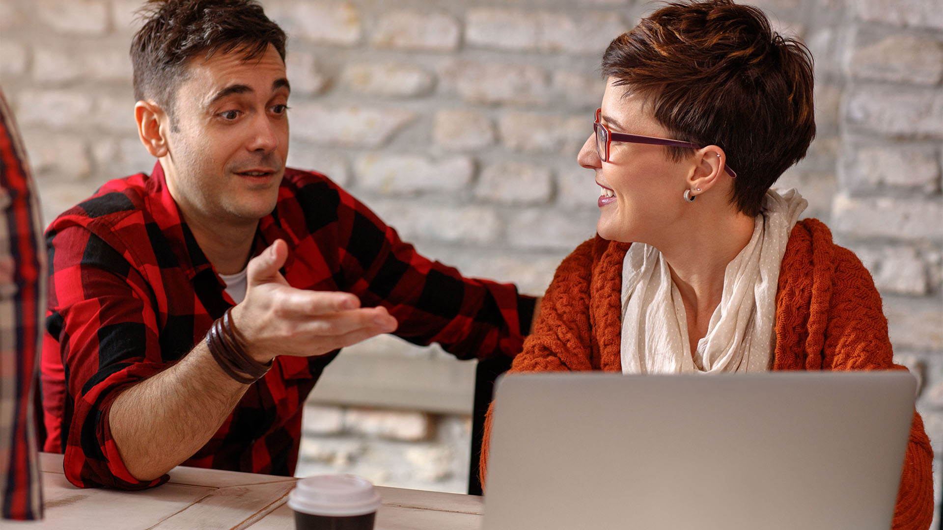 Young male and female colleagues in studio talking and working at laptop